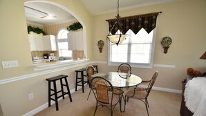 A dining area with a glass table surrounded by wicker chairs, a hanging light fixture, and a window with blinds. - 431 Wedgewood (North Myrtle Beach)