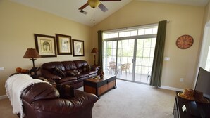 A living room with a brown leather couch, a coffee table, a TV stand, and a large window with curtains. - 431 Wedgewood (North Myrtle Beach)