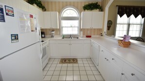 A kitchen with white cabinets, a window with a decorative arch, a tiled floor, and a refrigerator with magnets. - 431 Wedgewood (North Myrtle Beach)