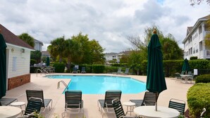 A swimming pool with lounge chairs and umbrellas, surrounded by greenery and buildings. - 214 Wedgewood (North Myrtle Beach)