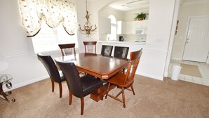 A dining room with a large wooden table surrounded by chairs, a chandelier, and a view into the kitchen. - 214 Wedgewood (North Myrtle Beach)