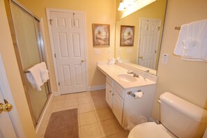 A bathroom with a white toilet, a sink, a mirror, and a shower area. - 2314 The Havens (North Myrtle Beach)