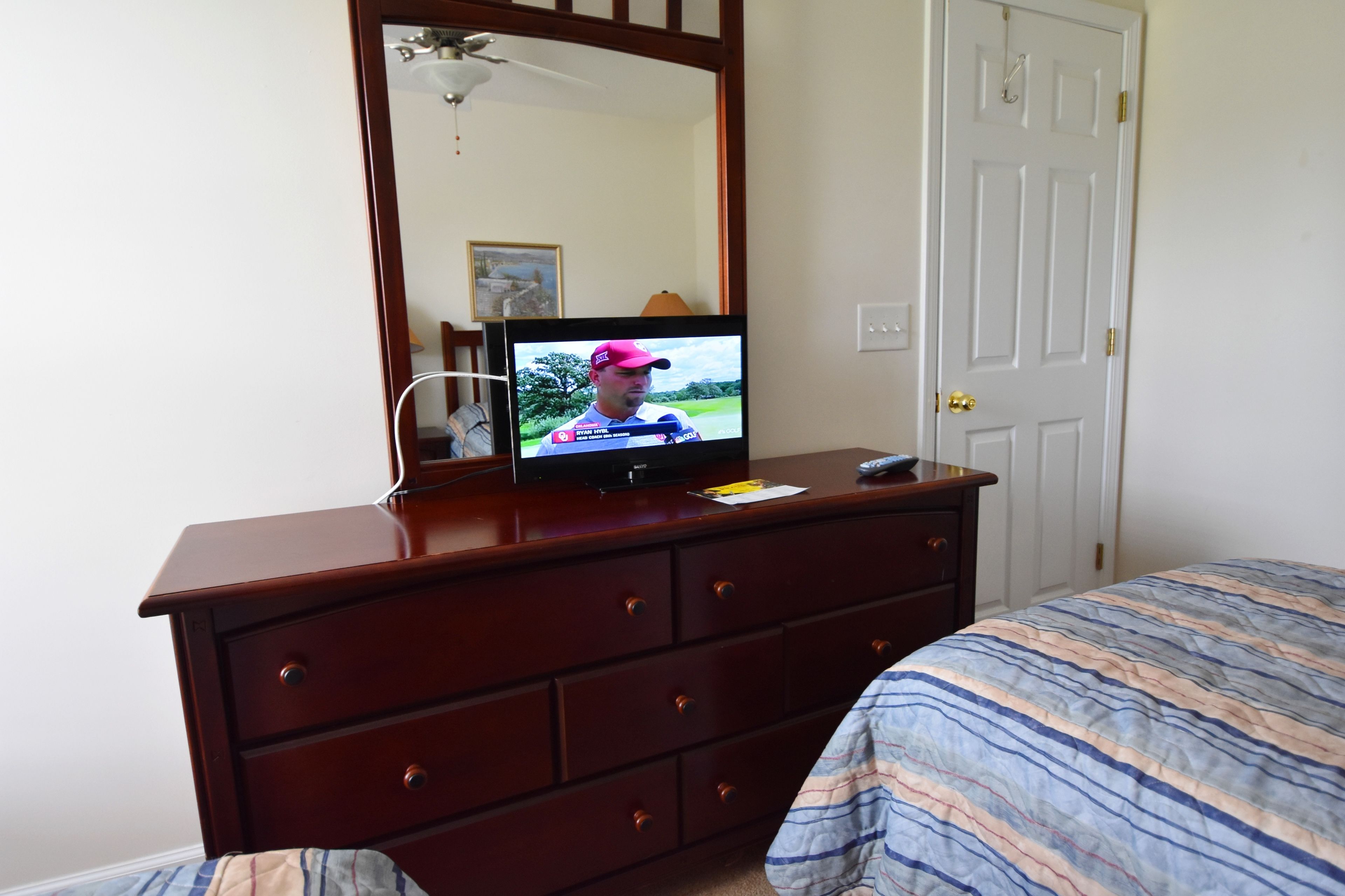 Une chambre avec une commode en bois, un téléviseur posé dessus, et un lit avec une literie à rayures.