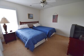 A bedroom with two beds, a ceiling fan, a nightstand with a lamp, a dresser, and an American flag on the wall. - 2314 The Havens (North Myrtle Beach)