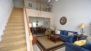 A spacious living room with a blue sofa, a wooden coffee table, and a staircase leading to a balcony. - 2314 The Havens (North Myrtle Beach)