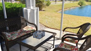 Un patio con muebles de mimbre y una mesa de vidrio, con vistas a un área cubierta de césped y un cuerpo de agua.