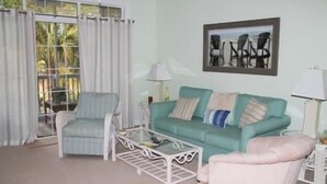 A living room with a teal sofa, a white armchair, and a glass coffee table. - 522 Cypress Bend (North Myrtle Beach)