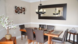 A dining area with a wooden table, six chairs, a chandelier, and wall art. - 327 The Havens (North Myrtle Beach)