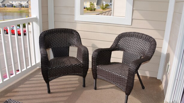 A porch with two wicker chairs, a view of a lake, and a glimpse of a red car in the background. - 327 The Havens (North Myrtle Beach)