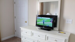 A white dresser with a flat-screen TV displaying a golf game, a door, and a light switch on the wall. - 622 Willow Bend (North Myrtle Beach)