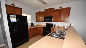 A kitchen with wooden cabinets, a black refrigerator, a microwave, a stove, and a sink. - 722 Willow Bend (North Myrtle Beach)