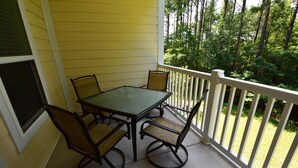 A covered patio with a table and four chairs, surrounded by a white railing, overlooking a grassy area with trees. - 722 Willow Bend (North Myrtle Beach)