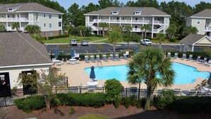 A pool area with lounge chairs and umbrellas, surrounded by a fence and palm trees. - 722 Willow Bend (North Myrtle Beach)