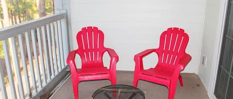A balcony with two red chairs and a small round table.