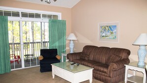A living room with a glass coffee table, striped sofa, two white side tables, and a painting on the wall.