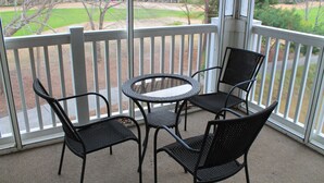A balcony with a round table and four chairs, overlooking a grassy area with trees and buildings. - 534 Wedgewood (North Myrtle Beach)