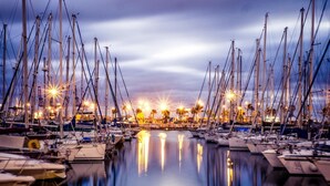 Un puerto deportivo con numerosas embarcaciones amarradas en aguas tranquilas, que reflejan las luces de los alrededores.
