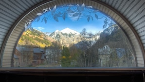 A view through a window with a floral design, featuring a mountain landscape, trees, and buildings.