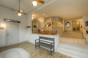 A spacious living area with a bench, a dining table, and a kitchen area visible through an archway.