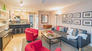 A modern apartment with a kitchen, dining area, and living room. It includes a sofa, red chairs, and a coffee table.