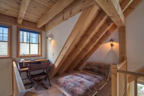 Une chambre à coucher aménagée dans un espace sous les toits, avec un plafond en pente, un bureau, une chaise et un lit.