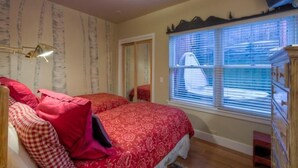 A bedroom with two beds, a dresser, a window with blinds, and a ceiling light.