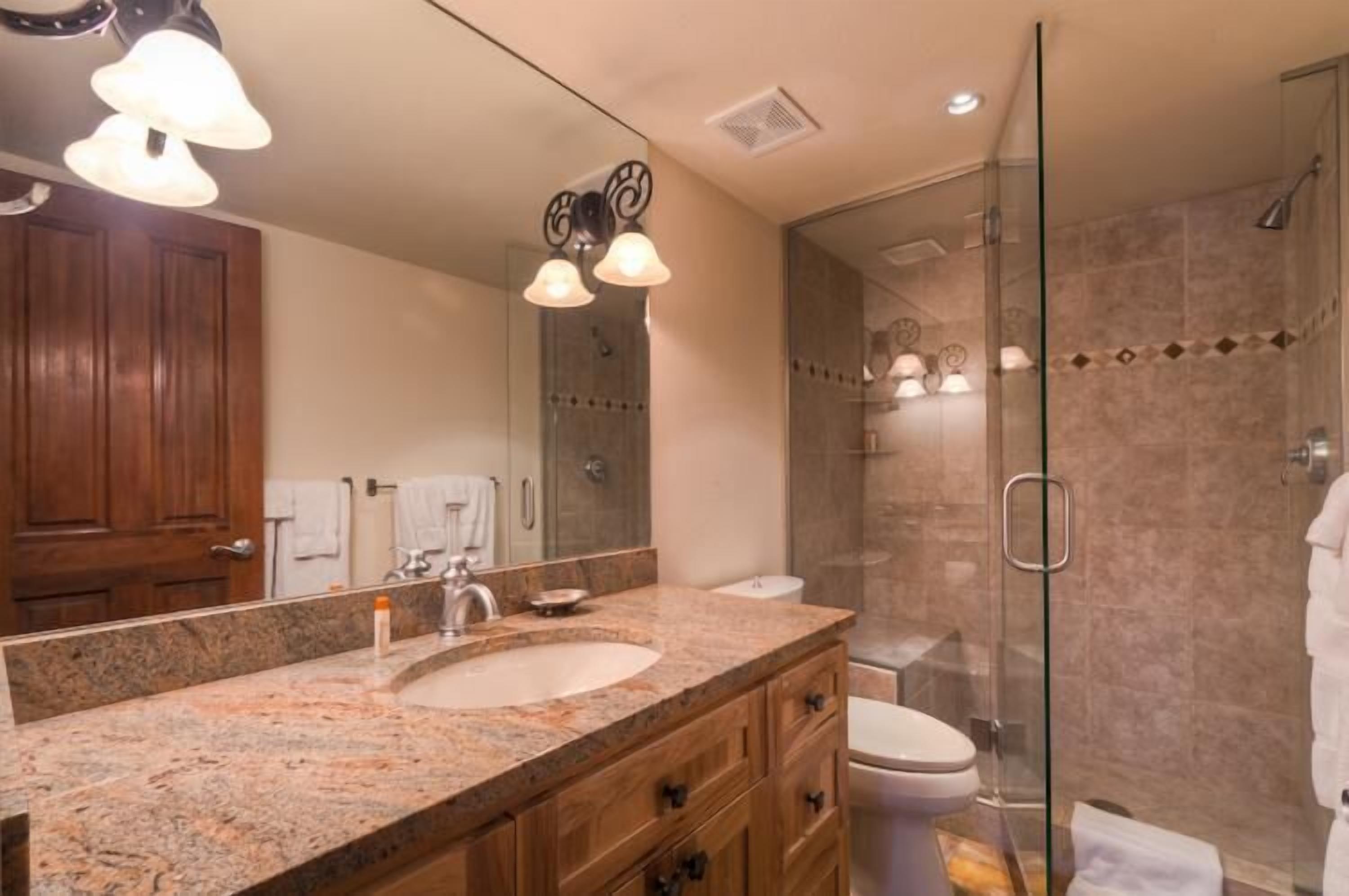 Un baño moderno con lavamanos de granito, un espejo grande, cerramiento de ducha de vidrio y muebles de madera.
