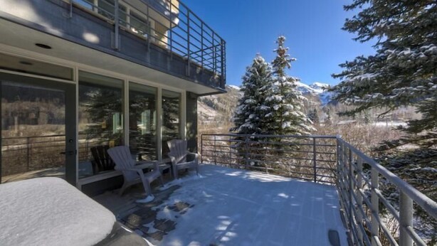 A modern building with a glass balcony, snow-covered ground, and a snow-covered tree in the background. - Muscatel Flats 2 1 Bedroom Condo By Accommodations in Telluride (Telluride)