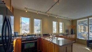 A modern kitchen with a large island, wooden cabinets, and a view of snowy mountains through the windows. - Muscatel Flats 2 1 Bedroom Condo By Accommodations in Telluride (Telluride)