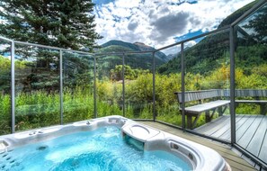 A hot tub with a mountain view, surrounded by glass walls and a wooden deck. - Muscatel Flats 4 1 Bedroom Condo By Accommodations in Telluride (Telluride)