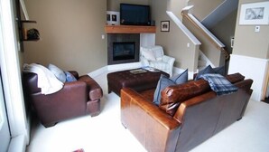 Een woonkamer met een open haard, een televisie en een trap.