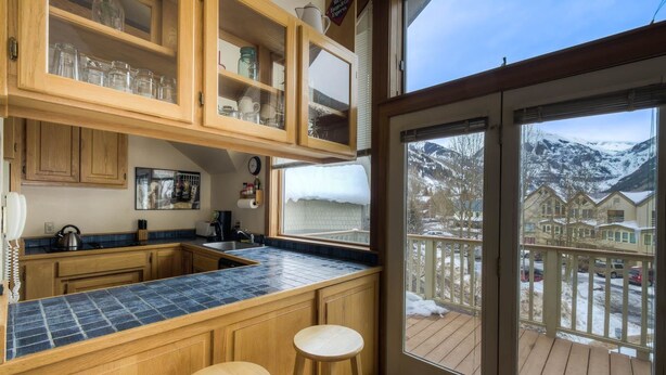 A kitchen with wooden cabinets, a blue tiled countertop, and a view of a snowy mountain landscape through a glass door. - Plunge H 3 Bedroom Condo By Accommodations in Telluride (Telluride)