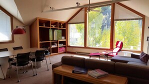 A modern living room with a large window, a dining area, and a built-in bookshelf. - Plunge H 3 Bedroom Condo By Accommodations in Telluride (Telluride)