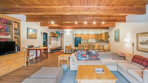 Un salon chaleureux avec un plafond en bois, une télévision, un canapé, une table basse et un coin repas comprenant une table et des chaises.