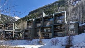 Un chalet à plusieurs étages doté de balcons, un paysage enneigé et une rivière au premier plan.