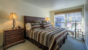 Une chambre avec un grand lit, deux lampes de chevet, une commode en bois et une chaise près de la fenêtre.
