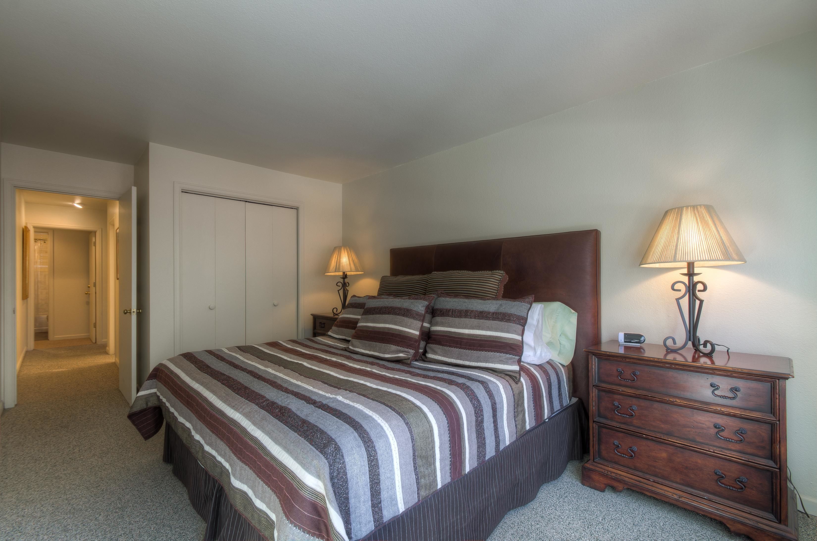 A bedroom with a bed, bedside lamps, a dresser, and a door leading to another room.