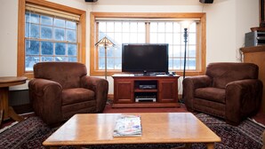 A living room with two brown armchairs, a wooden coffee table, a flat-screen TV on a wooden stand, a lamp, and a window with a view of mountains. - Sundance 302 2 Bedroom Condo By Accommodations in Telluride (Telluride)