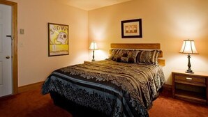 A bedroom with a large bed, two bedside tables with lamps, a door, and a wall with a framed picture and a poster. - Sundance 302 2 Bedroom Condo By Accommodations in Telluride (Telluride)