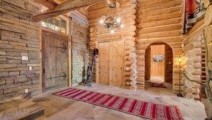 A log cabin interior with a stone wall, wooden log walls, a red patterned rug, and a wooden door. - Rocky Road Retreat 4 Bedroom Holiday home By Accommodations in Telluride (Telluride)