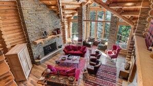 A log cabin interior with a stone fireplace, red sofas, and a large window overlooking greenery. - Rocky Road Retreat 4 Bedroom Holiday home By Accommodations in Telluride (Telluride)