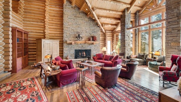A log cabin interior with a fireplace, wooden furniture, and a large window. - Rocky Road Retreat 4 Bedroom Holiday home By Accommodations in Telluride (Telluride)