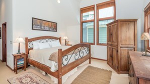 Une chambre à coucher avec un lit en bois, deux tables de chevet avec des lampes, une grande armoire en bois et un tableau accroché au mur.