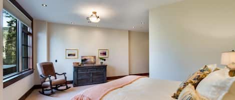 A bedroom with a large bed, a dresser, a rocking chair, and a window.