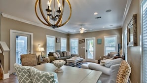 A spacious living room with a chandelier, a dining table, and multiple seating areas.