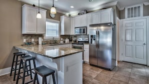 A kitchen with white cabinets, a stainless steel refrigerator, a microwave, a stove, and a large island with bar stools.