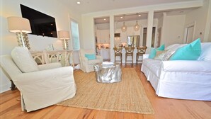 A living room with a sofa, armchair, and a coffee table. There is a kitchen area visible in the background. - Wine Down Retreat 4 Bedroom Holiday Home By Coastal Dreamin (Santa Rosa Beach)
