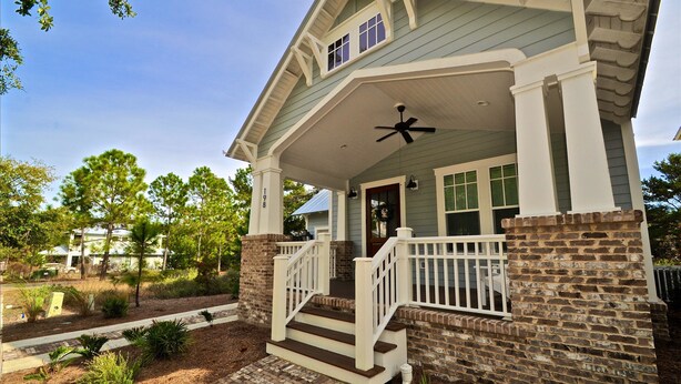 A two-story house with a covered porch, a brick exterior, and a white railing. - Wine Down Retreat 4 Bedroom Holiday Home By Coastal Dreamin (Santa Rosa Beach)