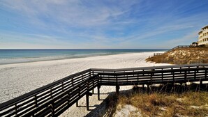 A beach with a wooden boardwalk leading to a building with a balcony overlooking the ocean. - Wine Down Retreat 4 Bedroom Holiday Home By Coastal Dreamin (Santa Rosa Beach)