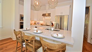 A modern kitchen with white cabinetry, stainless steel appliances, and a central island with seating. - Wine Down Retreat 4 Bedroom Holiday Home By Coastal Dreamin (Santa Rosa Beach)